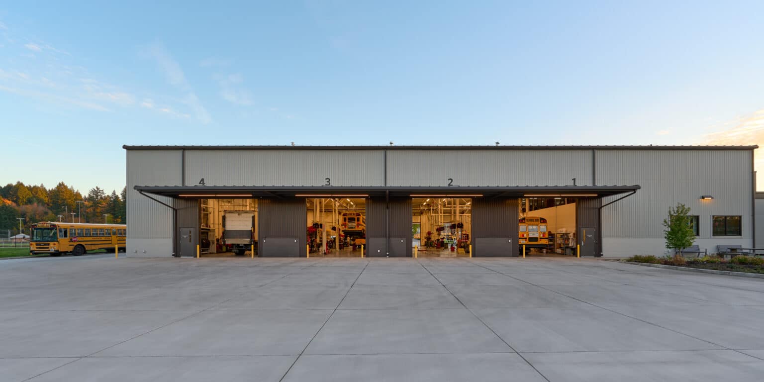 Exterior view of a modern transportation facility with large garage doors and a spacious concrete driveway.