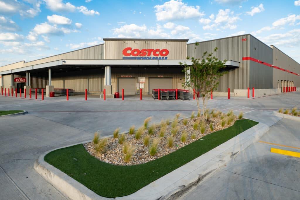 Front of a tan warehouse building with large red and blue Costco sign under a blue sky with clouds.