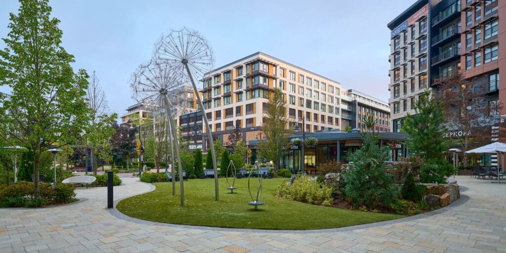 Modern urban park surrounded by mid-rise apartment buildings with art sculptures and green landscaping.